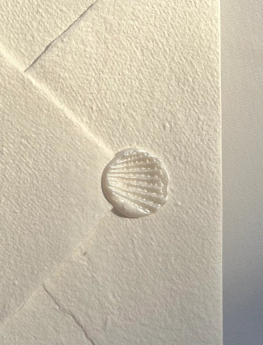 A white pearl recycled paper envelope with a white wax seashell seal. A welcoming initiation to this store, coastal and exclusive vibes.  