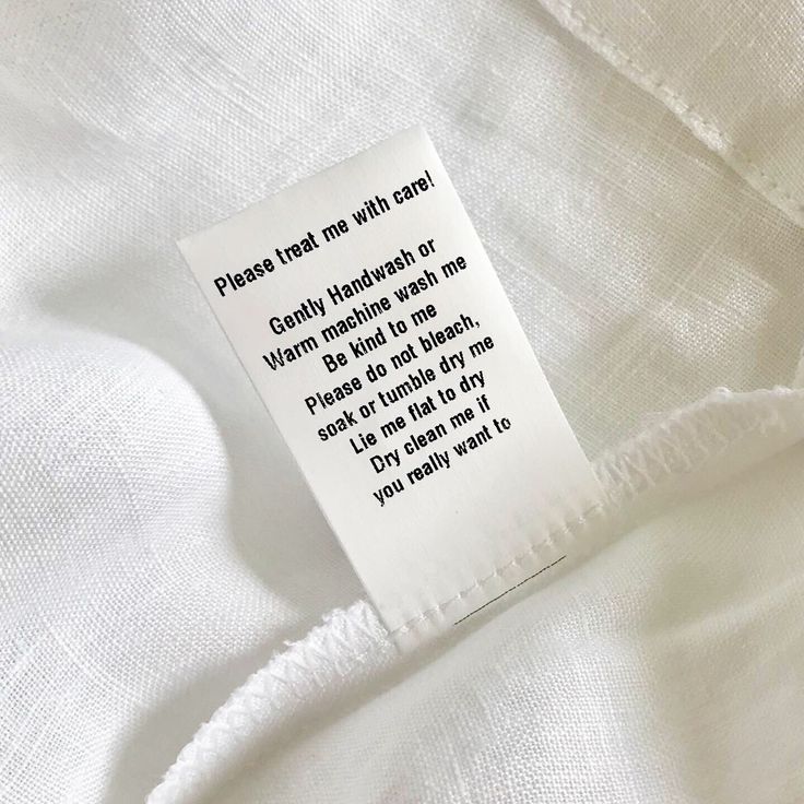 a delicate white fabric, featuring a tag that reads. Please treat me with care! Gently Hand wash or warm machine wash me, be kind to me, please do not bleach , soak or tumble dry me. Lie me flat to dry, dry clean me if you really want to. Just invoking the importance of caring for your children's clothing to make it last. 